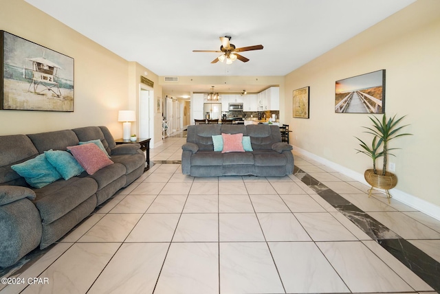 living room featuring ceiling fan with notable chandelier, light tile patterned floors, baseboards, and visible vents