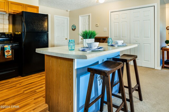 kitchen featuring a textured ceiling, black appliances, a center island, light wood-type flooring, and a kitchen bar