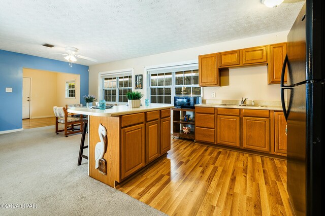 kitchen with a textured ceiling, a kitchen island, light hardwood / wood-style flooring, black appliances, and ceiling fan