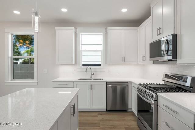 kitchen with sink, appliances with stainless steel finishes, decorative light fixtures, white cabinetry, and light wood-type flooring