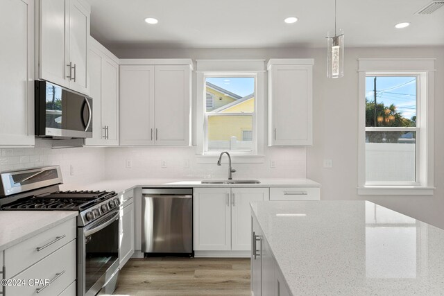 kitchen with sink, white cabinets, backsplash, stainless steel appliances, and light wood-type flooring