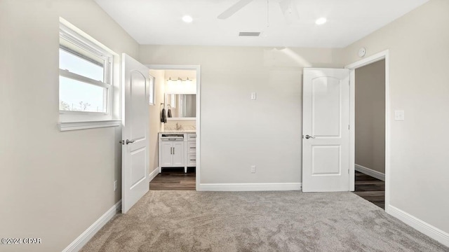 unfurnished bedroom featuring ensuite bath, ceiling fan, and dark colored carpet