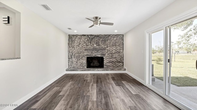 unfurnished living room with ceiling fan, brick wall, a brick fireplace, and hardwood / wood-style floors