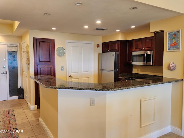 kitchen with dark stone counters, kitchen peninsula, white fridge, light tile flooring, and cooktop