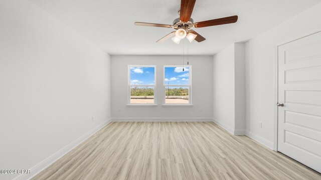 spare room featuring light wood finished floors, ceiling fan, and baseboards