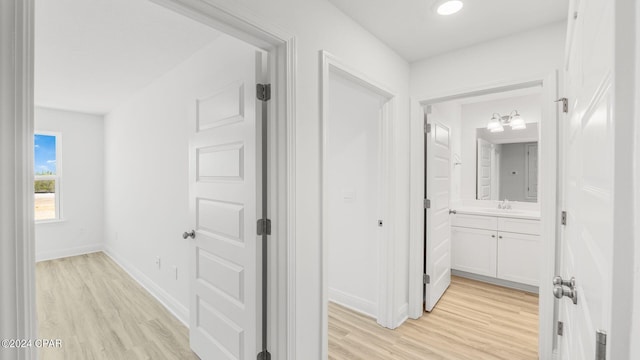 corridor with baseboards, light wood-style floors, and a sink