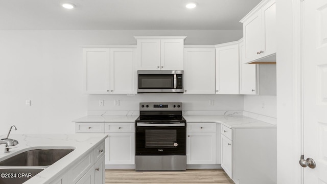 kitchen with light wood-type flooring, a sink, light stone counters, stainless steel appliances, and white cabinets