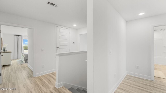 corridor featuring baseboards, an upstairs landing, visible vents, and light wood-style flooring