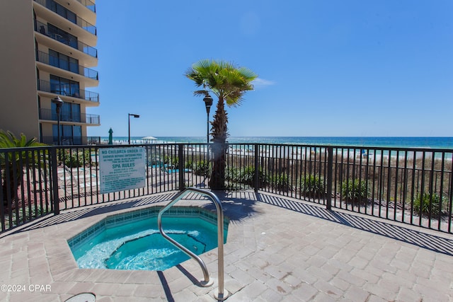 view of pool with a community hot tub, a water view, and a beach view