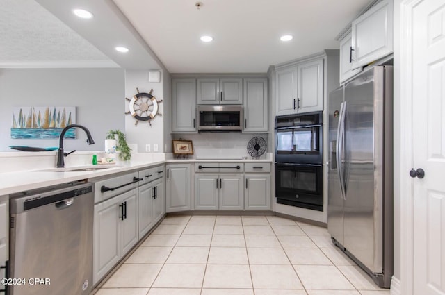 kitchen with crown molding, gray cabinetry, stainless steel appliances, sink, and light tile floors