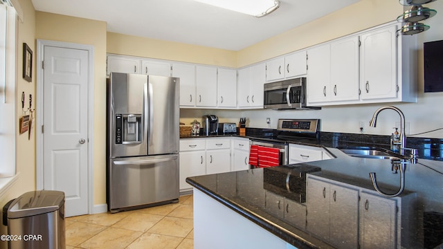 kitchen with appliances with stainless steel finishes, sink, dark stone countertops, white cabinets, and light tile patterned flooring