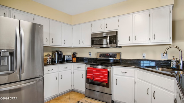 kitchen with stainless steel appliances, dark stone counters, white cabinetry, and sink