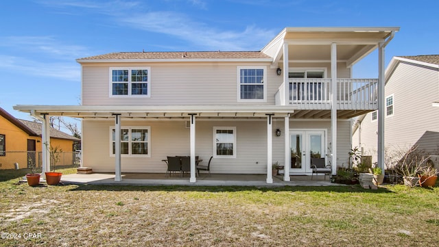 rear view of property featuring a balcony, french doors, a lawn, and a patio