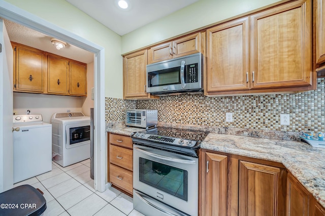 kitchen with light stone counters, light tile patterned floors, tasteful backsplash, appliances with stainless steel finishes, and washer and dryer