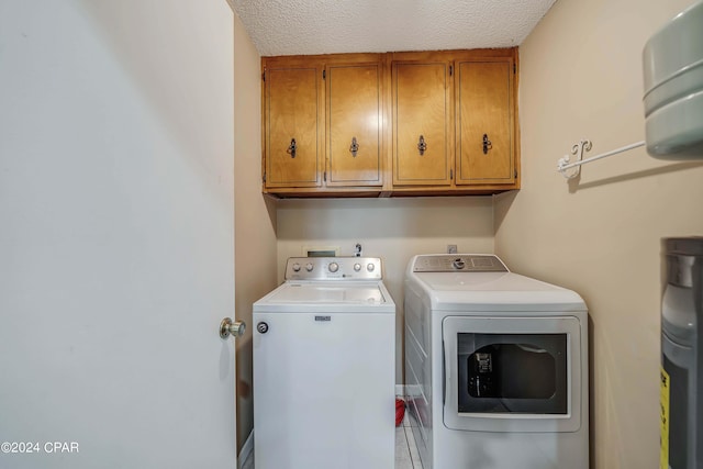 laundry area with a textured ceiling, separate washer and dryer, light tile patterned floors, and cabinets