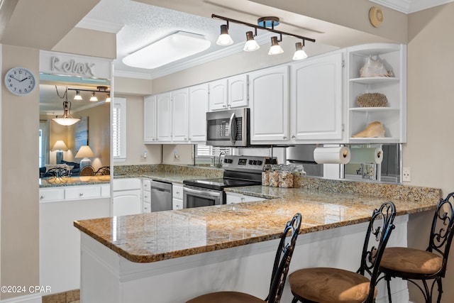 kitchen with stainless steel appliances, a breakfast bar, kitchen peninsula, white cabinetry, and light stone counters