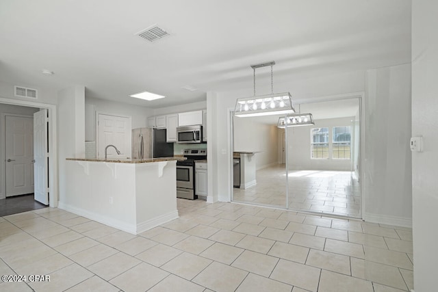 kitchen featuring white cabinetry, decorative light fixtures, stainless steel appliances, light tile floors, and a breakfast bar area