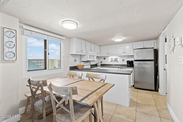 kitchen featuring stove, dishwashing machine, white cabinetry, light tile floors, and stainless steel fridge