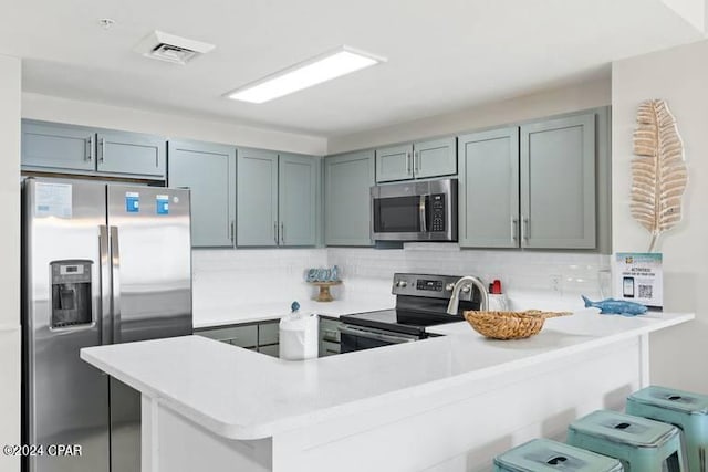 kitchen featuring appliances with stainless steel finishes, a breakfast bar area, a peninsula, light countertops, and backsplash