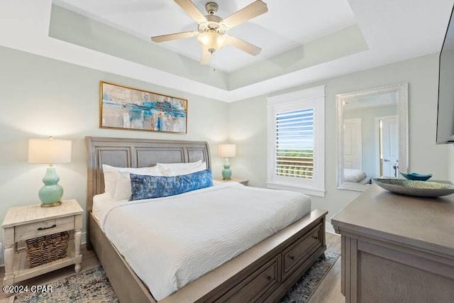 bedroom with ceiling fan, a tray ceiling, and light wood-type flooring