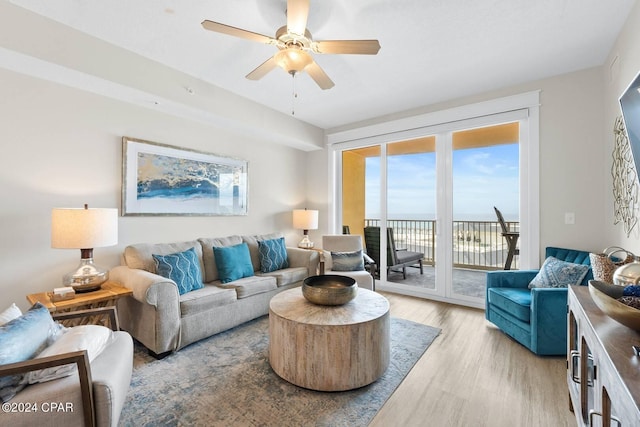 living area featuring light wood-type flooring, a ceiling fan, and a water view