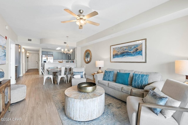 living room with light wood-style floors, baseboards, and ceiling fan with notable chandelier