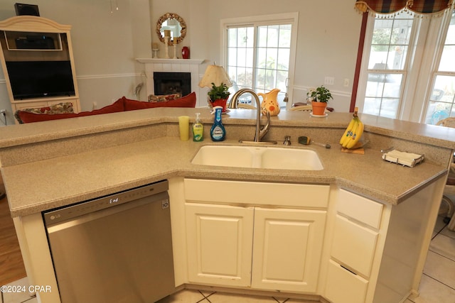 kitchen featuring dishwasher, a tile fireplace, light tile floors, sink, and white cabinetry