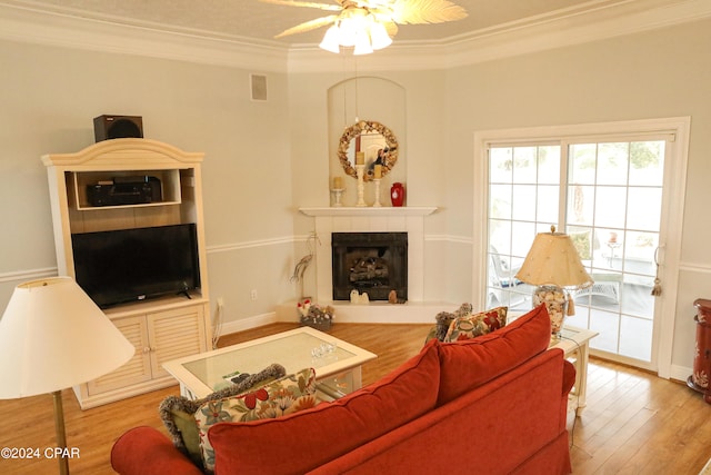 living room featuring ornamental molding, a tiled fireplace, ceiling fan, and hardwood / wood-style floors