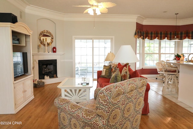 living room featuring crown molding, a tiled fireplace, ceiling fan, and hardwood / wood-style floors