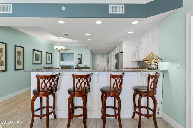 kitchen with an inviting chandelier, kitchen peninsula, ornamental molding, white cabinetry, and stainless steel refrigerator