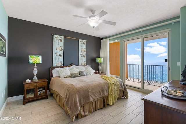 bedroom featuring access to exterior, ceiling fan, a water view, and a textured ceiling