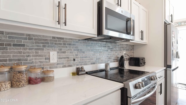 kitchen featuring appliances with stainless steel finishes, white cabinetry, backsplash, and light stone counters