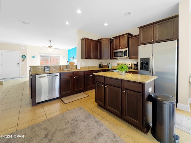 kitchen with a kitchen island, ceiling fan, appliances with stainless steel finishes, and light stone counters