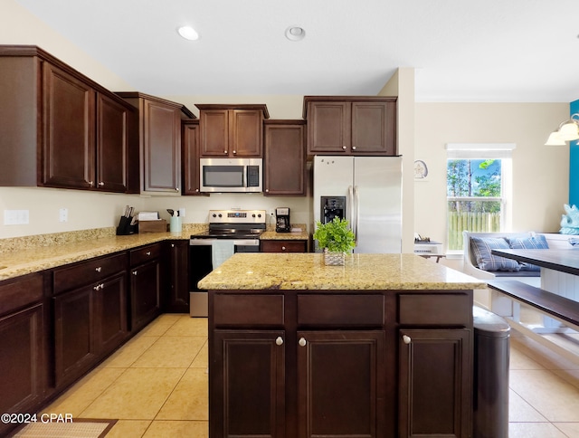 kitchen with light tile floors, a kitchen island, light stone countertops, appliances with stainless steel finishes, and dark brown cabinetry