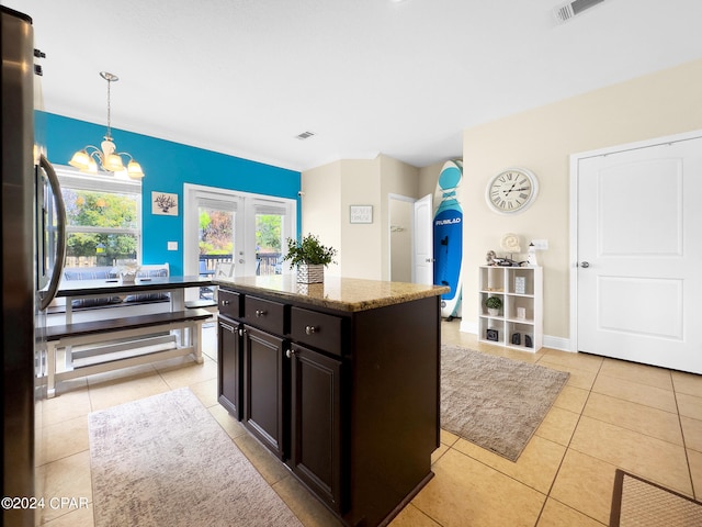 kitchen with pendant lighting, a notable chandelier, black refrigerator, french doors, and light stone counters