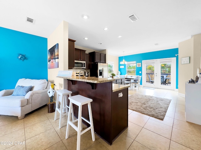 kitchen featuring french doors, dark brown cabinets, stainless steel appliances, light stone countertops, and hanging light fixtures