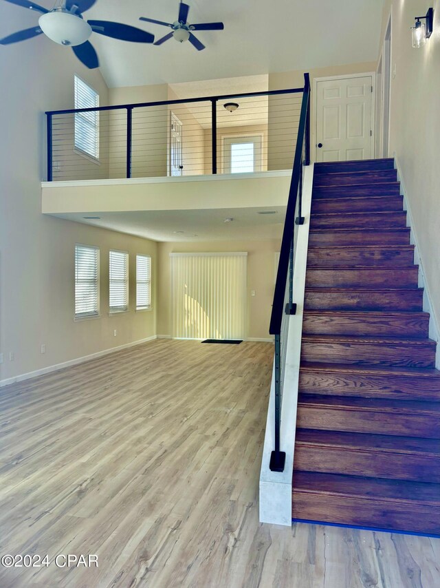 stairs with a high ceiling, ceiling fan, and wood-type flooring