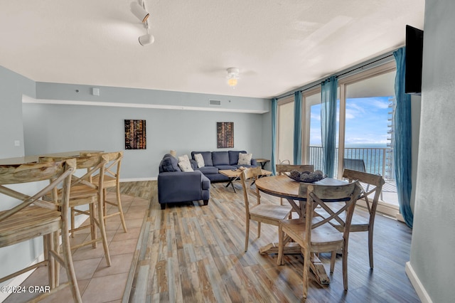 dining space featuring expansive windows, a water view, light wood-type flooring, a textured ceiling, and rail lighting