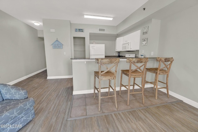 kitchen featuring kitchen peninsula, white appliances, wood-type flooring, a kitchen bar, and white cabinetry