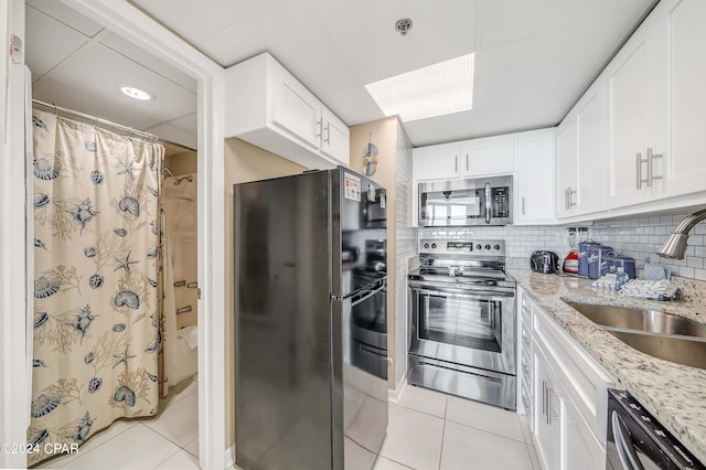 kitchen with appliances with stainless steel finishes, tasteful backsplash, light tile floors, and light stone counters