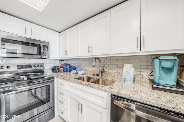 kitchen with white cabinetry, stainless steel appliances, sink, light stone counters, and tasteful backsplash