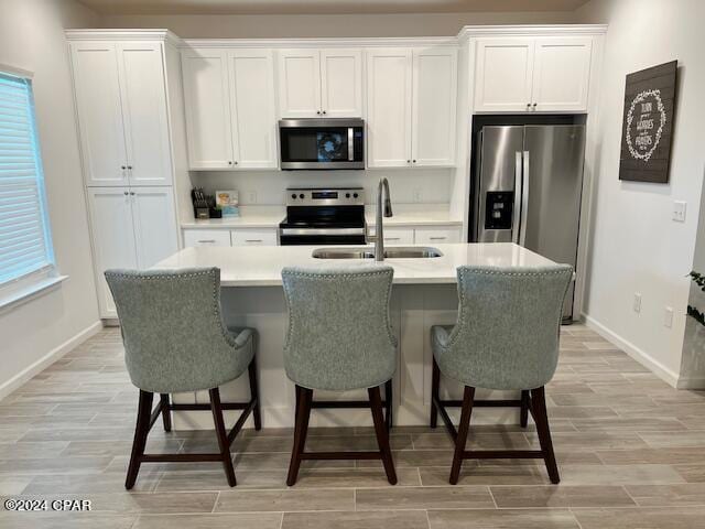 kitchen with stainless steel appliances, a sink, white cabinets, wood tiled floor, and an island with sink