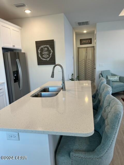 kitchen featuring a sink, visible vents, white cabinets, stainless steel refrigerator with ice dispenser, and a large island with sink