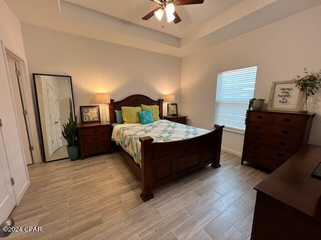 bedroom featuring a ceiling fan, a raised ceiling, baseboards, and light wood finished floors