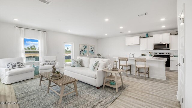 kitchen with white cabinetry, sink, light hardwood / wood-style floors, a center island with sink, and appliances with stainless steel finishes