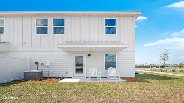 back of house with a patio area, central AC unit, board and batten siding, and a lawn