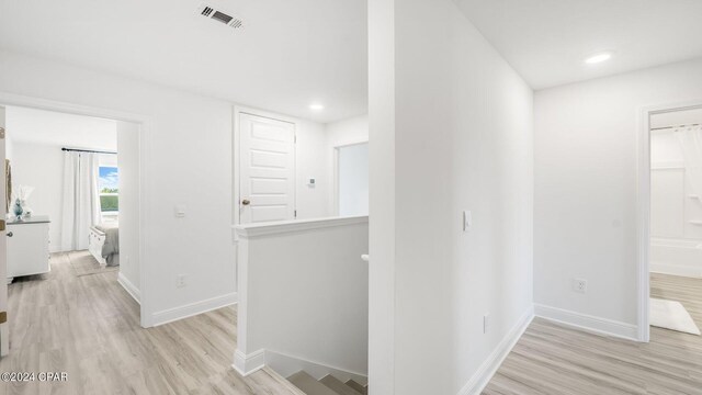 hallway with an upstairs landing, visible vents, light wood-style flooring, and baseboards