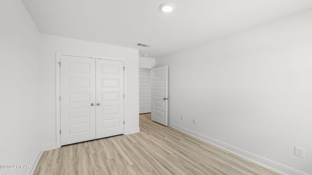 unfurnished bedroom with a closet, visible vents, light wood-style floors, and baseboards