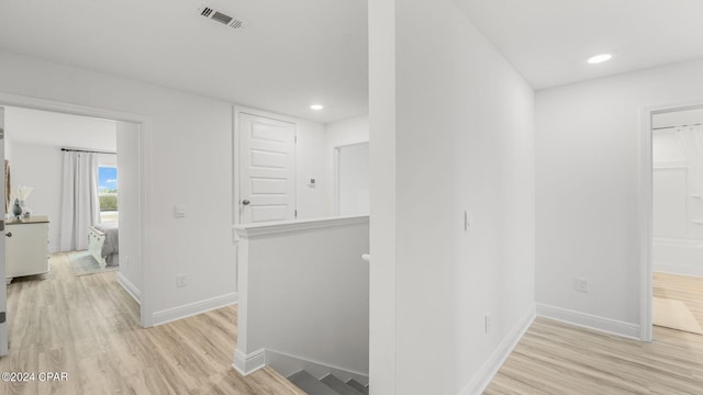 hallway with visible vents, an upstairs landing, baseboards, and light wood finished floors