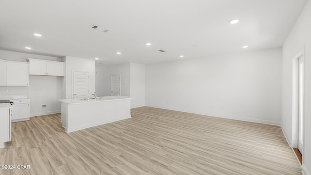 kitchen featuring white cabinetry, sink, light hardwood / wood-style floors, and a kitchen island with sink